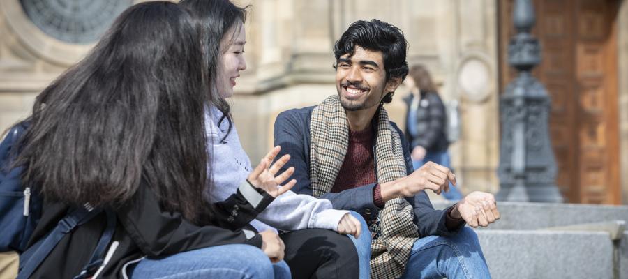 A group of students sit on the steps outside McEwan Hall, smiling whilst conversing