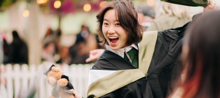 A graduating student grins at the camera whilst posing in their robes