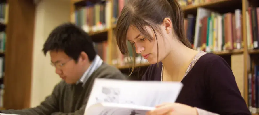 Two students are studiously reading books in the library