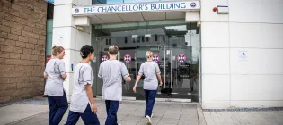 Four nursing students walk towards the Chancellor's Building in their nursing student uniforms