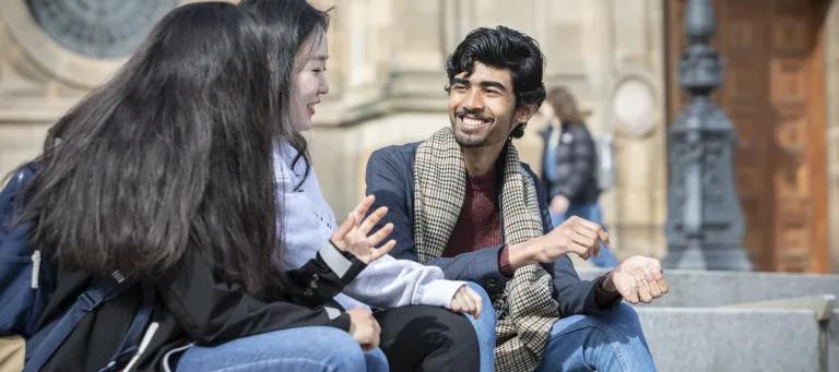 A group of students sit on the steps outside McEwan Hall, smiling whilst conversing