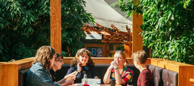 A group of students are sat round a table in Potterrow, a student union venue, smiling and chatting together