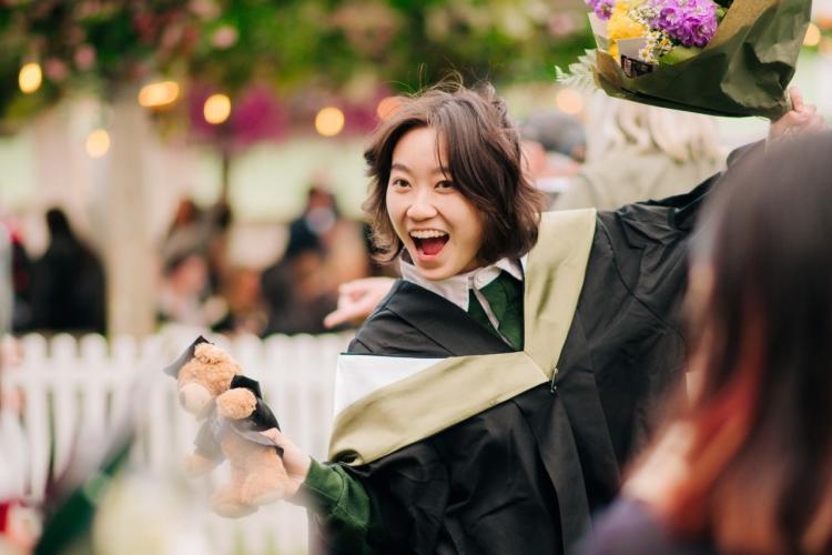 A graduating student grins at the camera whilst posing in their robes