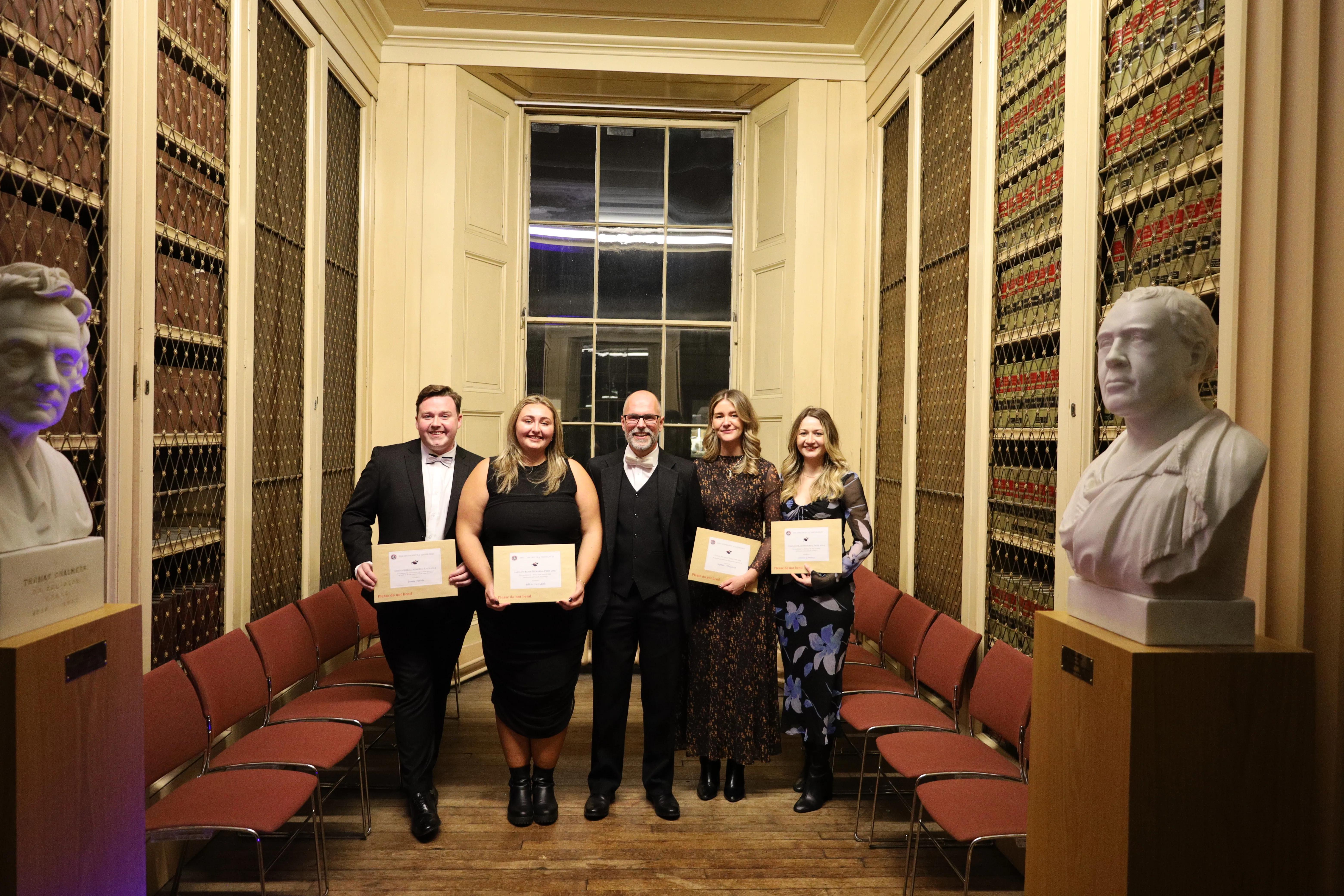 A group of graduates stand with their award certificates, smiling in celebration.