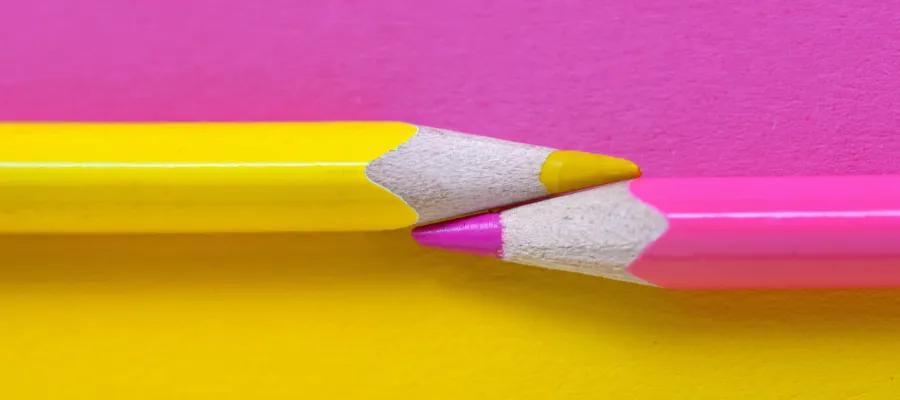 Shocking pink and yellow pencils pointing to each other on a shocking pink and yellow background