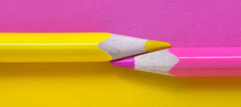 Shocking pink and yellow pencils pointing to each other on a shocking pink and yellow background
