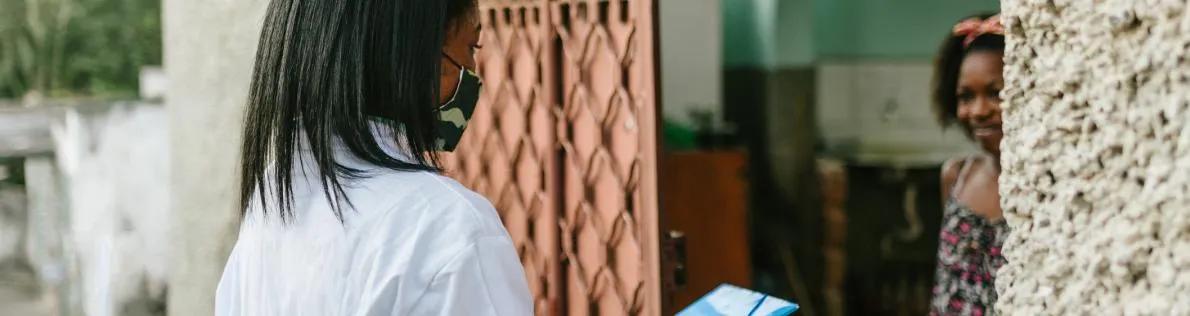 Female healthcare worker at the door of a young woman's home in Africa