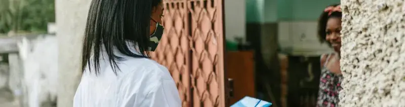 Female healthcare worker at the door of a young woman's home in Africa