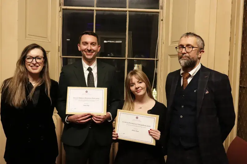The two award winners stand proudly smiling with their awards, flanked either side with an academic who teaches on their programme.