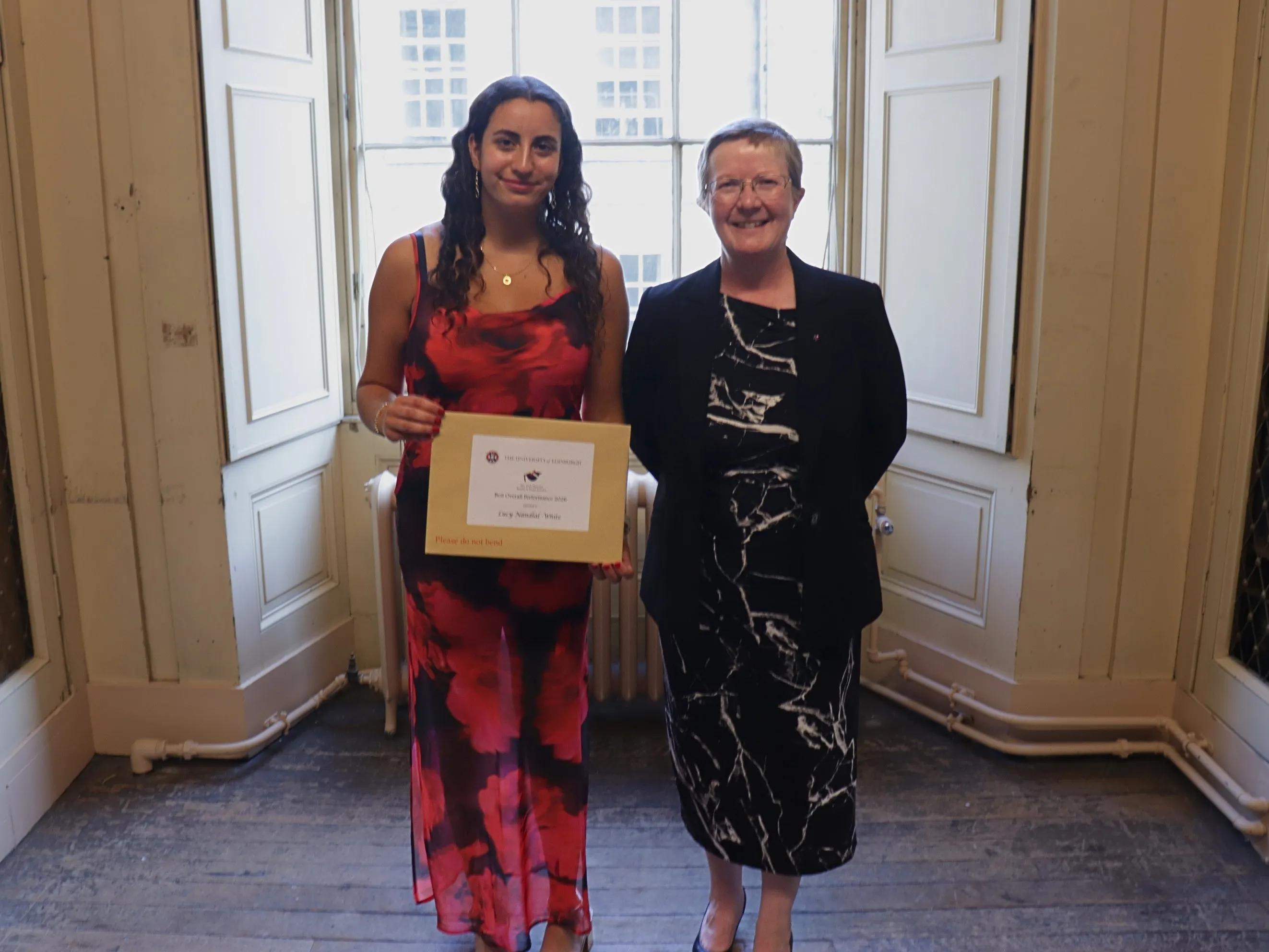 A proud graduate poses with their programme director, holding up their award certificate