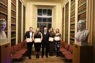 A group of graduates stand with their award certificates, smiling in celebration.