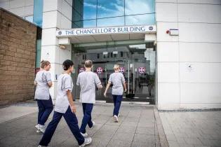 Four nursing students walk towards the Chancellor's Building in their nursing student uniforms