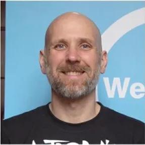 Sergio is smiling broadly at the camera with a welcome week sign behind him