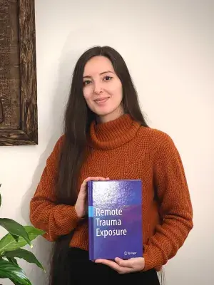 Dr Emily Pacheco stands proudly holding up her new book whilst smiling