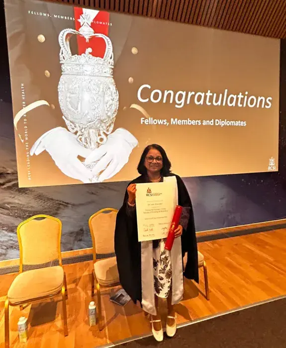 Dr Leah Macaden proudly holds up her award at the award ceremony, with a screen displaying the text Congratulations behind her.